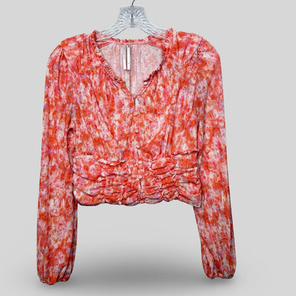 Anthropologie floral cropped top with long sleeves, ruching, and a ruffled hemline displayed on a white hanger.