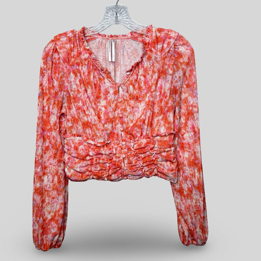  Anthropologie floral cropped top with long sleeves, ruching, and a ruffled hemline displayed on a white hanger.