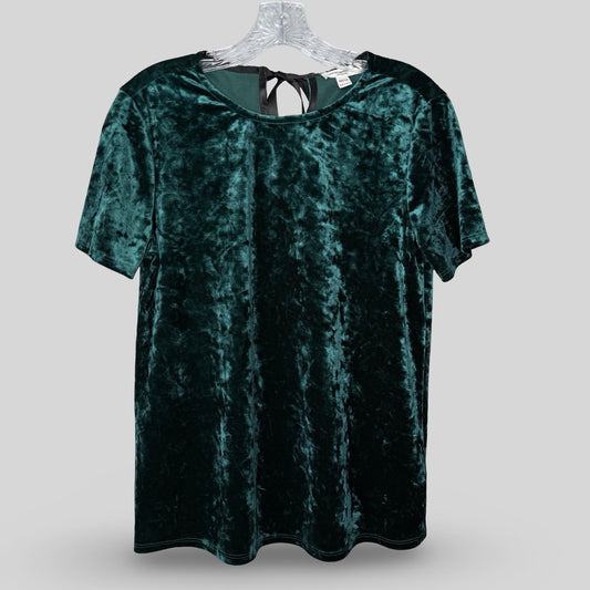 A short-sleeved green velvet tee with a black satin tie at the back of the neck, displayed on a hanger.