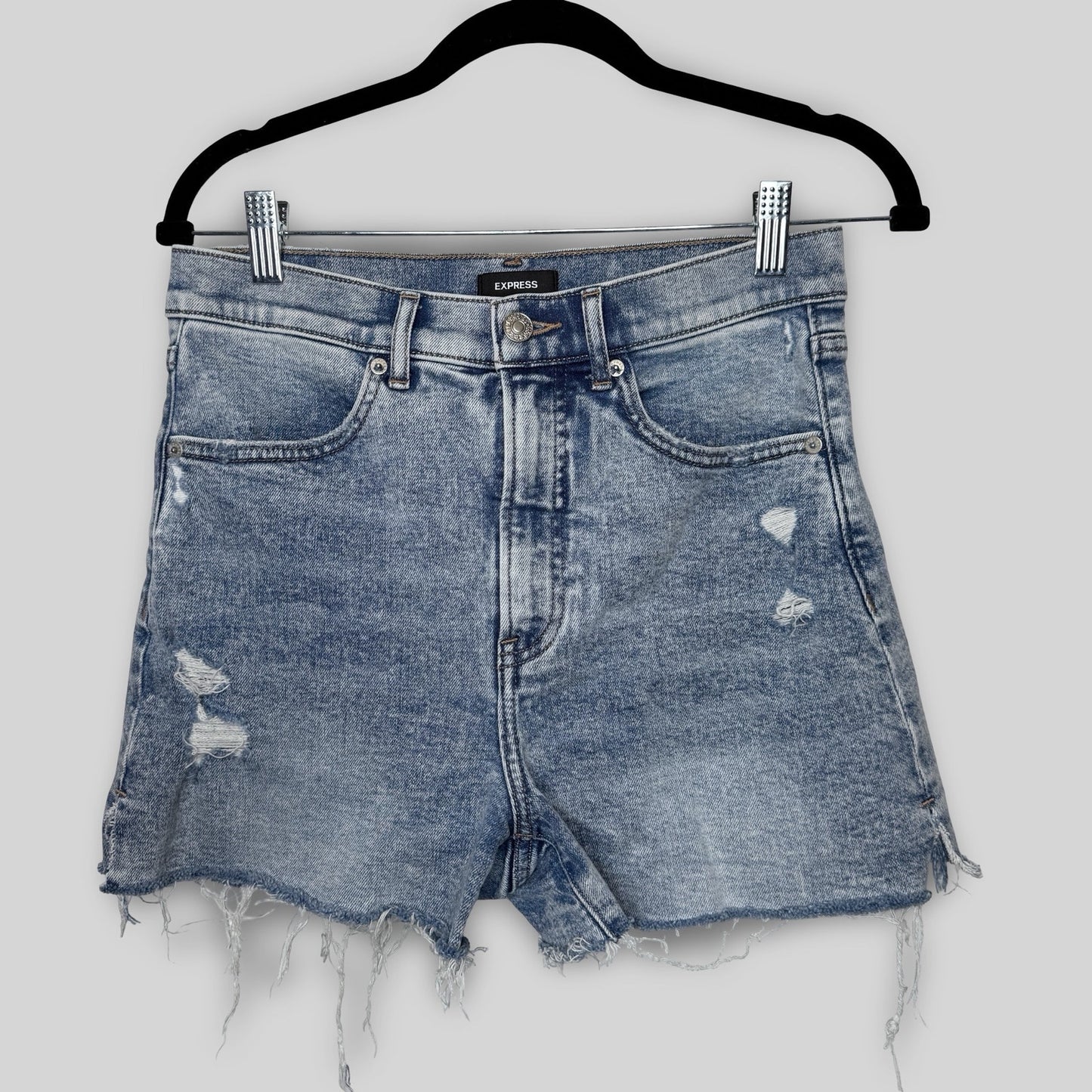 Blue denim shorts with distressed details on a hanger against a white background