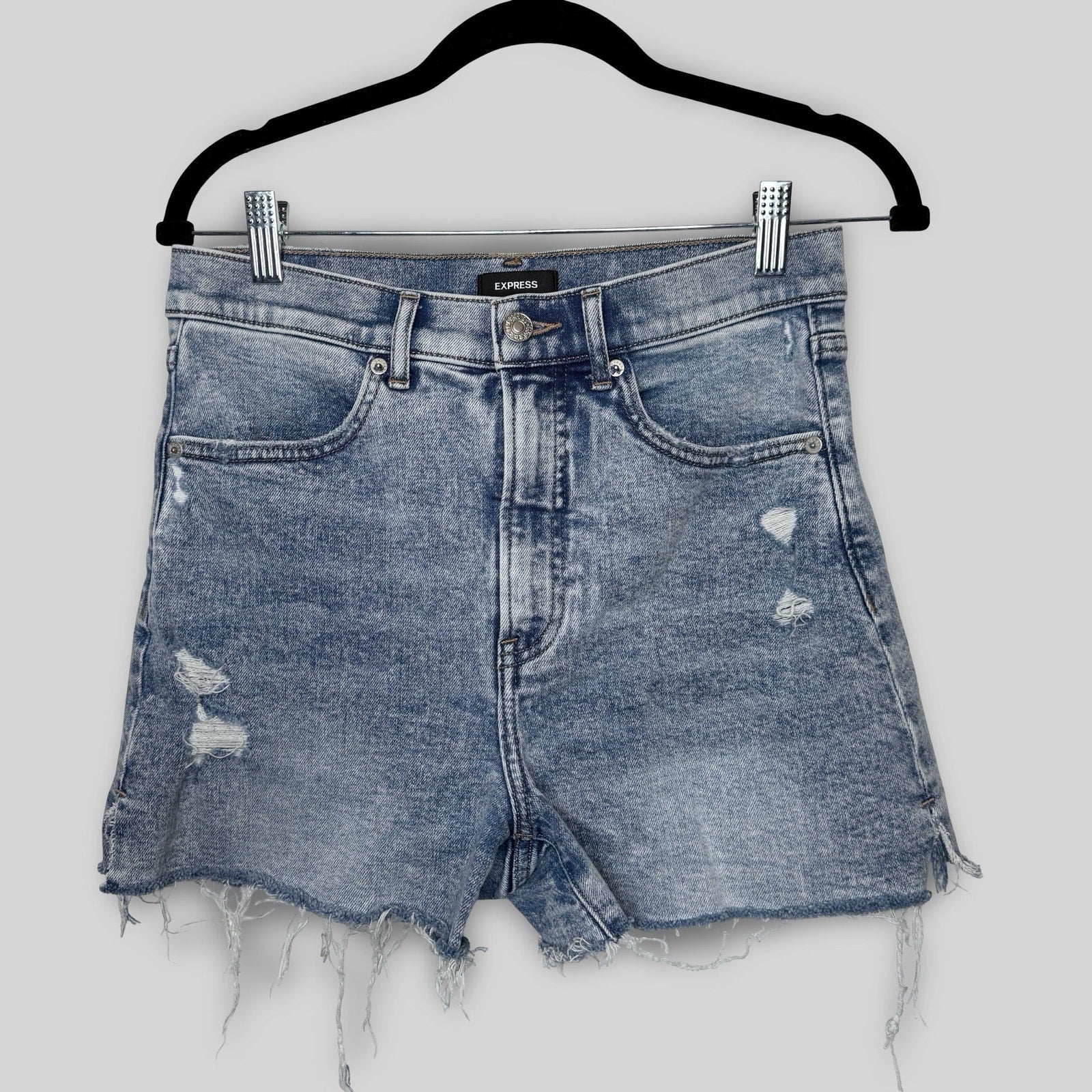 Blue denim shorts with distressed details on a hanger against a white background